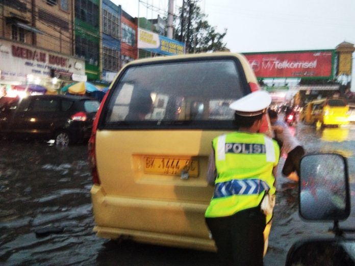 Polisi lalu lintas mendorong angkot yang mogok karena melewati banjir di Jalan Gatot Subroto persis di seputaran Plaza Medan Fair, Jumat (1/12/2017)